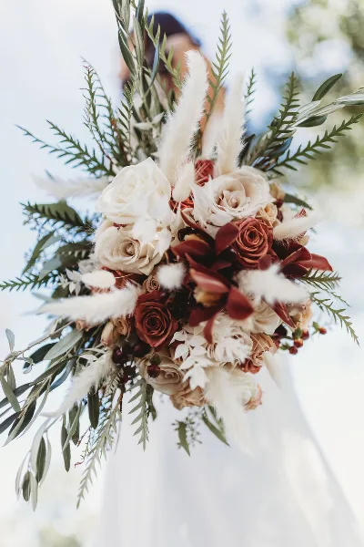 A close-up of a bridal bouquet featuring white and rust-colored roses, orchids, and greenery.