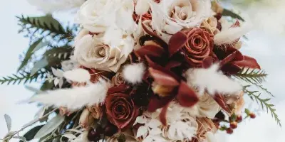 A close-up of a bridal bouquet featuring white and rust-colored roses, orchids, and greenery.