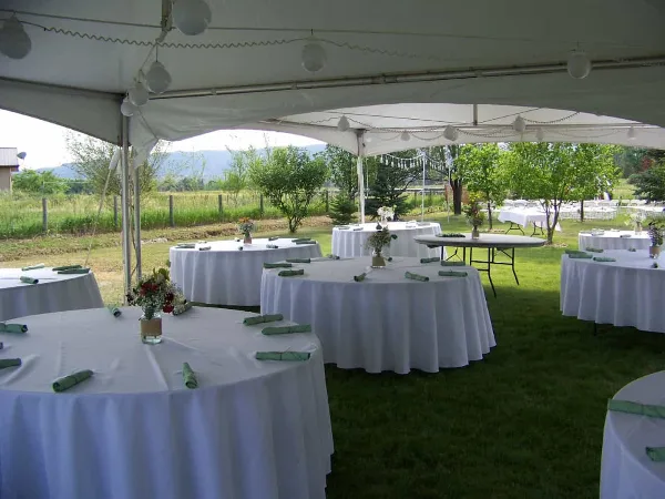 An outdoor event setup featuring a large white tent and several round tables with white tablecloths and green napkins.