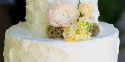 A two-tier white wedding cake decorated with pastel roses, ranunculus, and succulents.