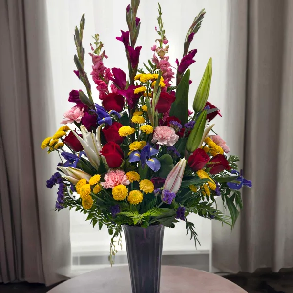 A tall mixed bouquet of roses, lilies, and colorful filler flowers in a purple vase