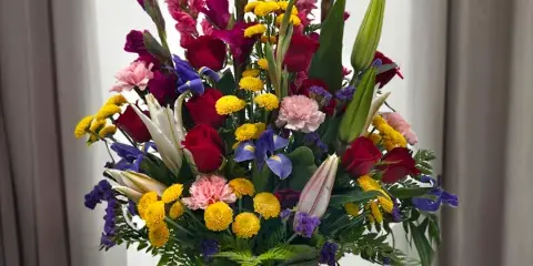 A tall mixed bouquet of roses, lilies, and colorful filler flowers in a purple vase