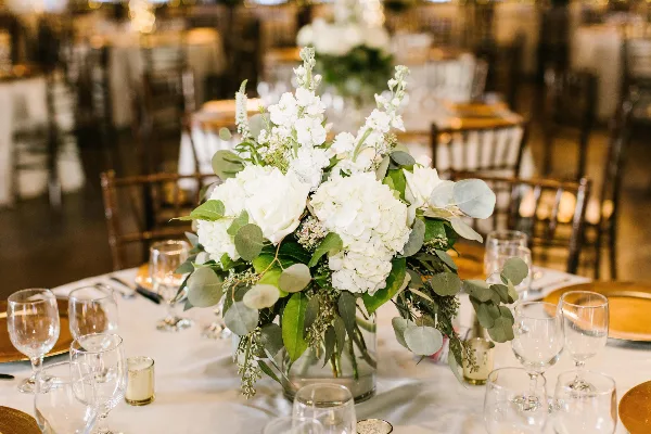 White wedding floral centerpiece with roses, hydrangeas, and eucalyptus on a reception table