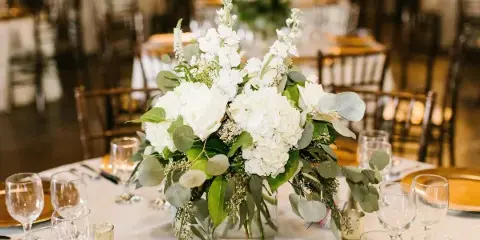 White wedding floral centerpiece with roses, hydrangeas, and eucalyptus on a reception table
