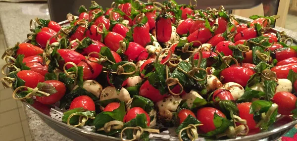 A large silver platter filled with a Caprese salad featuring cherry tomatoes, fresh mozzarella balls, and basil leaves.
