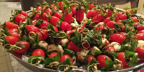 A large silver platter filled with a Caprese salad featuring cherry tomatoes, fresh mozzarella balls, and basil leaves.