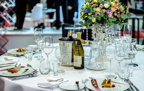 A formal dining table set with wine bottles, glasses, and plated food, typical of a catering service.
