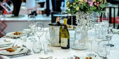 A formal dining table set with wine bottles, glasses, and plated food, typical of a catering service.