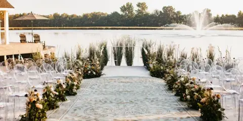A wedding ceremony aisle decorated with floral arrangements and greenery leading to a water feature.