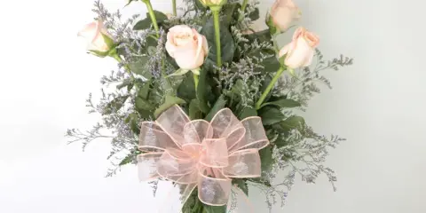 A floral arrangement featuring pale pink roses and greenery in a clear glass vase, accented with a large pink ribbon bow.