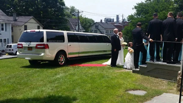 Bride and groom exit a white limousine onto a red carpet during a wedding event.
