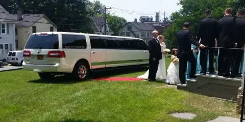 Bride and groom exit a white limousine onto a red carpet during a wedding event.