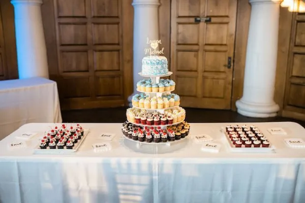 A wedding dessert table featuring a tiered stand of cupcakes and a small cake with a personalized topper.