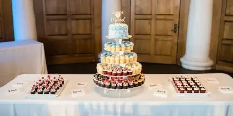 A wedding dessert table featuring a tiered stand of cupcakes and a small cake with a personalized topper.