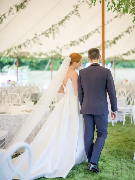 A bride and groom walking through a decorated wedding reception area with floral garlands and white tables.