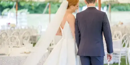A bride and groom walking through a decorated wedding reception area with floral garlands and white tables.
