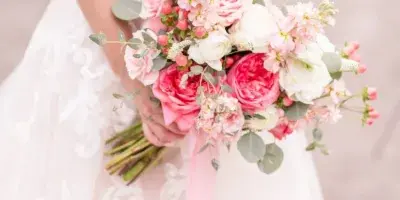 A bride in a white lace wedding dress holding a bouquet of pink and white roses with eucalyptus leaves.