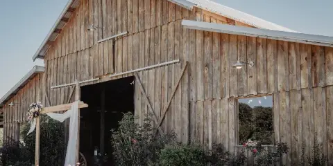 Exterior view of a rustic wooden barn wedding venue with a decorated archway and surrounding greenery.