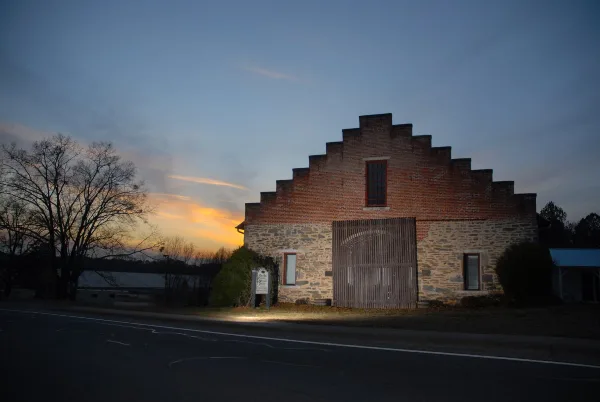Exterior view of a historic stone and brick barn with a stepped gable roof at dusk.