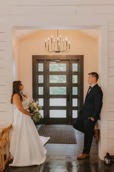 Bride and groom posing inside a white barn venue with a large wooden door and chandelier.