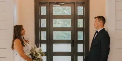 Bride and groom posing inside a white barn venue with a large wooden door and chandelier.