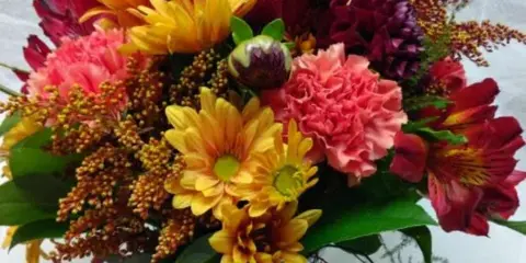 A vibrant mixed bouquet featuring red roses, yellow daisies, and pink carnations arranged in a clear glass vase.