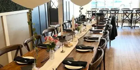 Long wooden table set for a meal in a restaurant with white balloons and string lights.