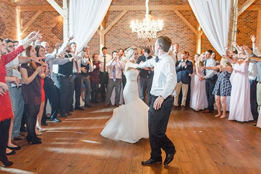 Bride and groom dancing at a wedding reception surrounded by celebrating guests.