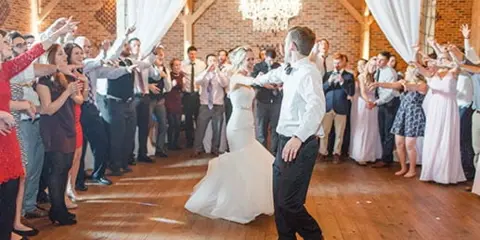 Bride and groom dancing at a wedding reception surrounded by celebrating guests.