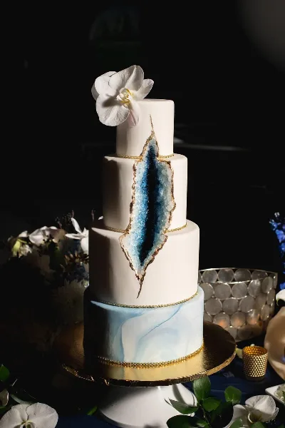 A four-tier white wedding cake featuring a blue crystal-like design and a white orchid on top.
