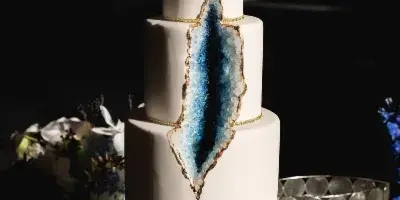 A four-tier white wedding cake featuring a blue crystal-like design and a white orchid on top.