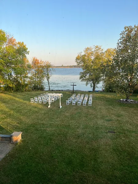 Outdoor wedding ceremony setup with white chairs on a grassy lawn facing a lake.