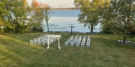 Outdoor wedding ceremony setup with white chairs on a grassy lawn facing a lake.