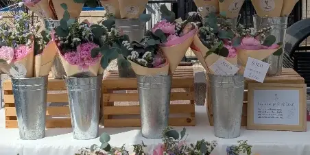 Rows of wrapped pink and white flower bouquets in metal buckets at a market table with a Walton Family Flowers banner.