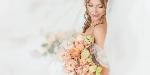 A bride in a white gown and veil holding a bouquet of pink, peach, and cream flowers.