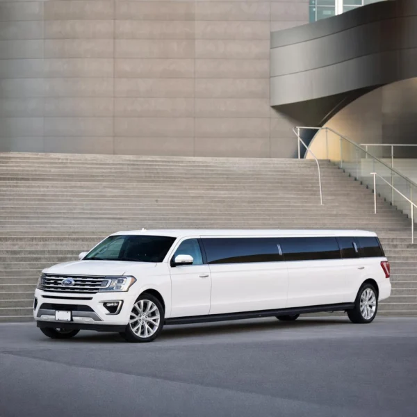 A white stretch limousine parked in front of a modern building with stone steps.