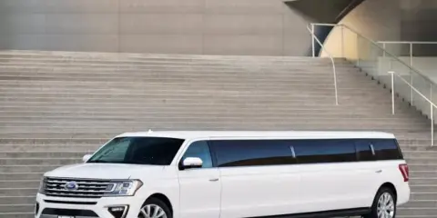 A white stretch limousine parked in front of a modern building with stone steps.