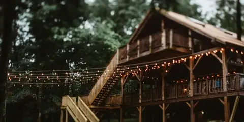 A large wooden venue building with a covered porch and string lights, surrounded by trees.