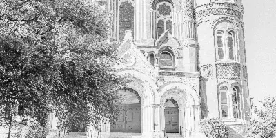 Black-and-white wedding photo of a bride and groom kissing beside a vintage car in front of a church.