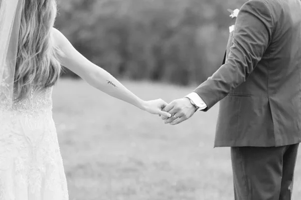 A black and white photograph of a bride and groom holding hands in an outdoor setting.