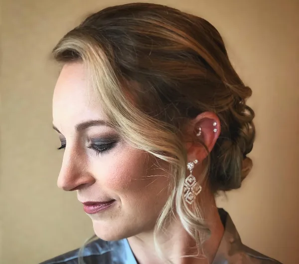 Profile view of a woman with an elegant updo hairstyle and professional makeup.