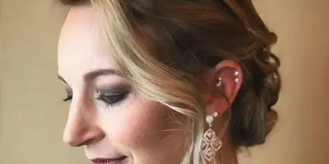 Profile view of a woman with an elegant updo hairstyle and professional makeup.