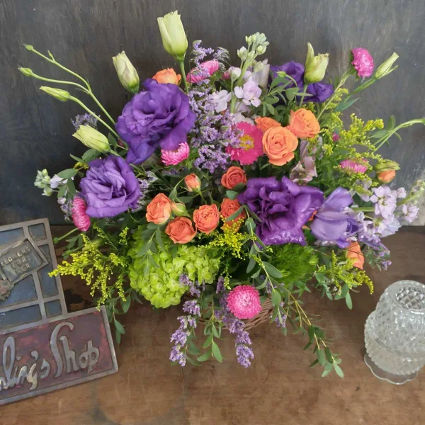 A colorful mixed bouquet of purple, pink, and orange flowers arranged in a basket.