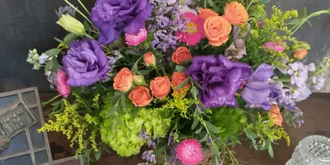 A colorful mixed bouquet of purple, pink, and orange flowers arranged in a basket.
