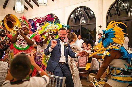 A groom and bride dancing at a wedding reception surrounded by guests and a brass band.