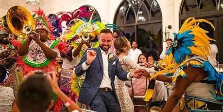 A groom and bride dancing at a wedding reception surrounded by guests and a brass band.