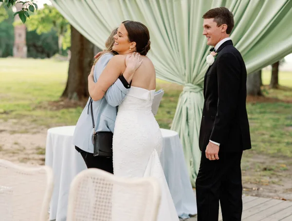 A bride and groom standing at an outdoor wedding ceremony with a green fabric backdrop.