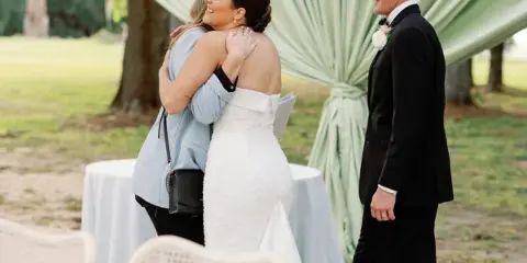 A bride and groom standing at an outdoor wedding ceremony with a green fabric backdrop.