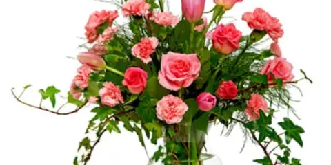 A floral arrangement featuring pink roses, carnations, and greenery in a clear glass vase.