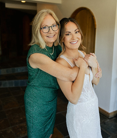 A smiling bride with styled hair and makeup posing with an older woman in a green dress.